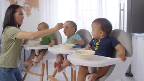 Asiatische-Mutter-Fütterung-Kleinkind-Triplets-in-Hochstühlen