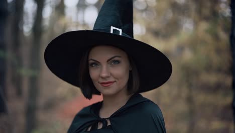 Beautiful-witch-in-cap,-long-dress,-mantle-on-autumn-forest-background.-Halloween-concept,-cosplay-dressing-up.-Slow-motion