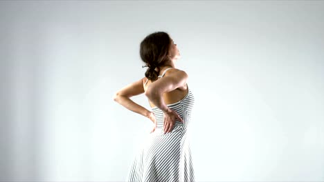 Young-female-with-lower-back-pain-rubbing-her-back-against-light-background