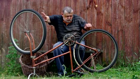 El-hombre-está-nervioso-por-la-bicicleta-muy-vieja-para-reparar-sentado-contra-la-valla-de-madera