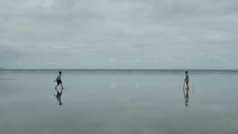 'Out'!-Two-young-boys-playing-beach-cricket,-the-bowler-hits-the-wicket!