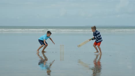 Zwei-Jungen-spielen-Strand-Cricket-einen-versuchen-zu-bekommen-und-die-anderen-Hits-die-Stümpfe!