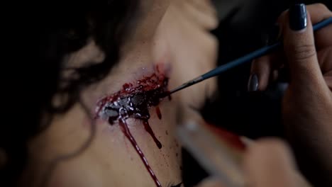 Make-up-artist-make-the-girl-halloween-make-up-in-studio.-Woman-applies-on-professional-greasepaint-on-the-girl-chest.-War-paint-with-blood,-scars-and-wounds.-Slow-motion