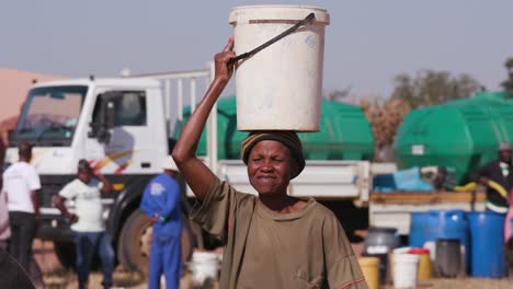 Zwei-afrikanische-Frau-Wasser-aus-Tankfahrzeugen-in-Kunststoffeimern-zu-sammeln-und-zu-Fuß-zurück-zu-ihren-Häusern