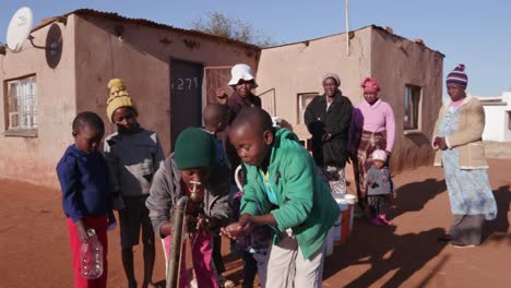 Niños-africanos-el-agua-potable-de-un-grifo-mientras-mujer-fila-para-recoger-el-agua-en-envases-de-plástico-debido-a-la-sequía-en-África-del-sur
