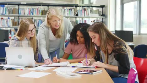 Tutor-trabajando-con-estudiantes-universitarios-de-mujer-en-biblioteca