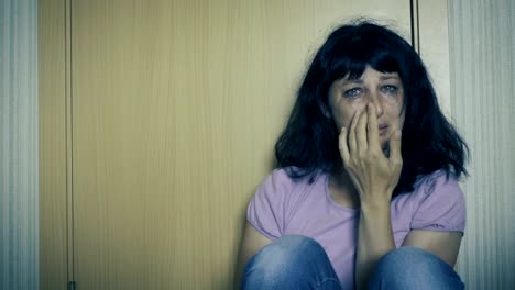 Violence-in-family.-Young-woman-is-crying-while-sitting-on-floor-in-corner-of-room.-Close-Up-Of-A-Scared-And-Crying-Woman-With-Smeared-Make-Up.-Girl-crying-in-corner-and-feeling-lonely.