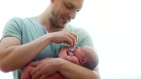 A-young-father-calms-a-newborn-baby-with-a-pacifier.-The-kid-takes-a-pacifier-in-his-mouth-and-sucks-it.-Neonatology.-Father's-Day.-Children's-Day