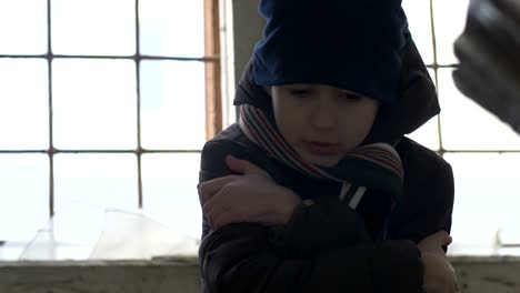 frozen-wary-boy-is-warming-in-a-dilapidated-old-house,-boy-standing-near-a-broken-window