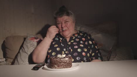 Senior-woman-watching-television-and-eating-cake-in-a-dark-room