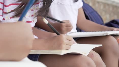 Asiatische-Schüler-zeichnen-in-Notebooks-auf-den-Knien-während-einer-Outdoor-Klasse