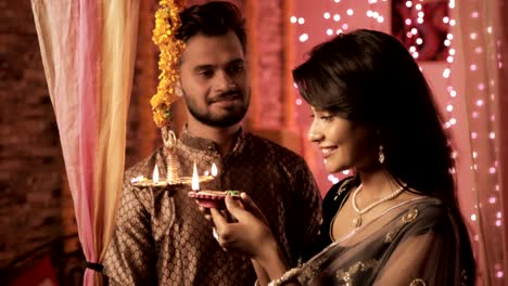attraktive-Frau-trägt-Sari-leuchtet-eine-Öllampe-während-Diwali-fest,-während-Mann-trägt-Kurta-mit-einem-Lächeln-blickt-auf