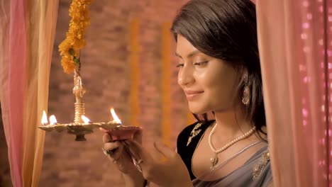 A-slow-mo-shot-of--happy-female-in-a-traditional-clothing-lights-a-hanging-metal-lamp-in-a-house-decorated-with-lights-and-flowers