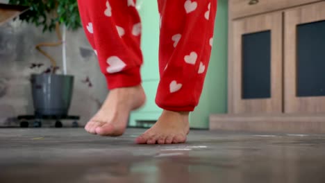 Cerrar-imágenes-de-piernas-de-mujer-bailando-descalza-sobre-piso-en-casa,-con-pantalones-de-pijama-rojo-divertido-en-corazones