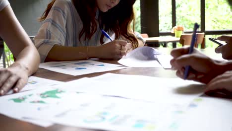 Close-up-of-Young-Asian-people-writing-and-preparing-their-presentation-papers-on-the-table-(underexposed-to-show-cinematic-look)