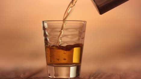 Verter-un-whisky-a-tiros-en-un-vaso-de-chupito-con-un-frasco-de-alcohol-de-cadera-metal,-primer-plano-macro