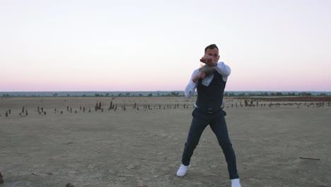 Mature-handwome-man-in-suit-with-long-gray-beard-boxing-with-shadow-outdoors-on-beach