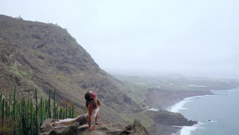 Mädchen-üben-von-Yoga-auf-den-Felsen-gegen-den-blauen-Himmel-und-das-azurblaue-Meer.-Frau-steht-auf-einem-Stein-in-einer-Brücke-Haltung.