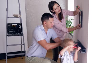 freundliche-Familie-mit-Kleinkind-Jungen-tun-renovieren-und-Schrauben-Regal-und-Bild-an-Wand