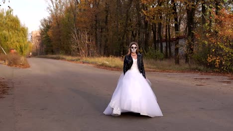 A-girl-in-a-wedding-dress-with-a-skull-mask-on-an-empty-road.-Halloween.