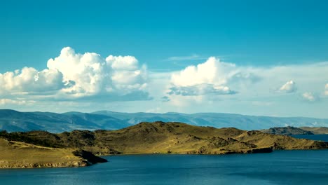 Weiße-Wolken-schweben-über-glatte-See-und-bergiges-Gelände.-Wolkengebilde.