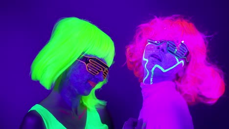 Langsame-Motin-von-schönen-sexy-Frauen-mit-fluoreszierenden-Make-up-und-Kleidung-Tanz-im-Neonlicht.-Night-Club,-Party-Konzept.