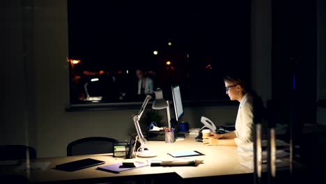 Good-looking-young-lady-is-working-overtime-using-computer-late-at-night-then-taking-off-glasses-and-rubbing-tired-temples,-eyes-and-face-then-drinking-coffee.