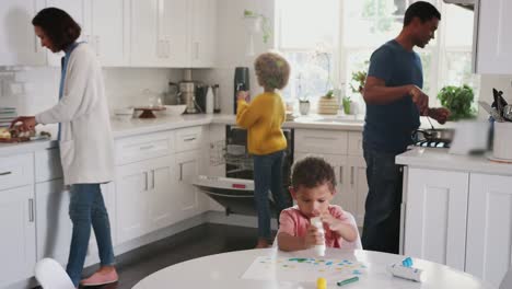 Junge-schwarze-Junge-malen-ein-Bild-in-der-Küche,-während-seine-Familie-Essen-im-Hintergrund-zubereitet