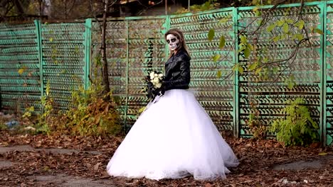 Creepy-bride-with-makeup-in-the-form-of-skull-on-the-background-of-an-old-fence.