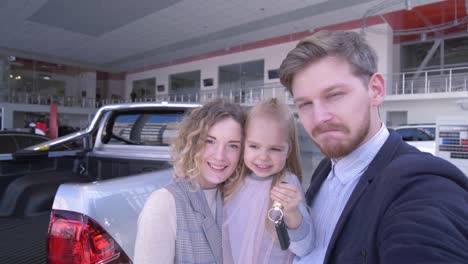 client-couple-with-cute-child-girl-with-keys-record-video-on-mobile-phone-near-new-purchased-car-in-auto-show