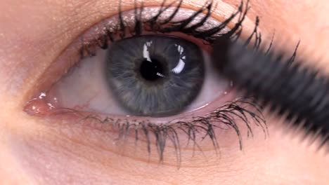 blue-eyed-woman-applying-mascara-closeup-macro