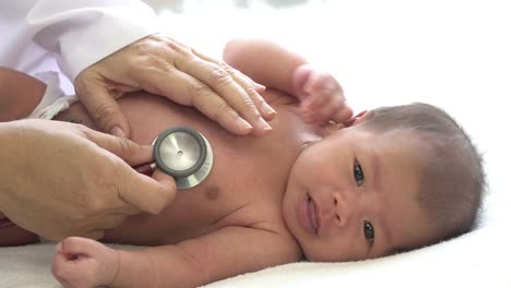 4K-Medium-close-up-shot-female-pediatrician-doctors-hand-comforting-asian-newborn-baby-girl-using-stethoscope-listening-to-little-baby-girl-heartbeat-for-medical-exam.-Hospital-nursery-healthcare-concept.