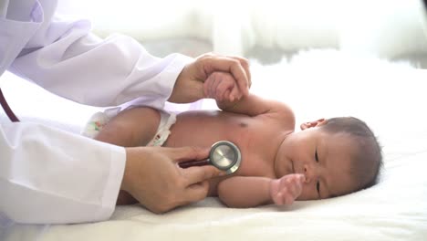 4K-Inyección-media-de-mujeres-pediatras-de-la-mano-sosteniendo-la-mano-de-niña-recién-nacida-asiática-y-usar-estetoscopio-escuchando-a-la-niña-pequeña-latidos-del-corazón-para-el-examen-médico.-Cuidado-de-la-guardería-del-hospital-y-concepto-de-me