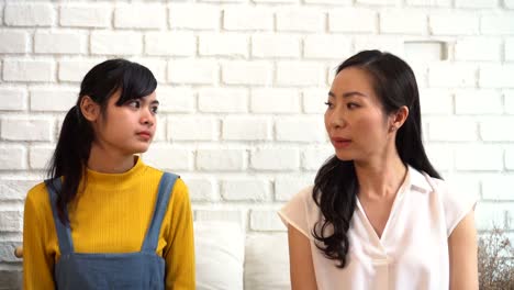 Displeased-Asian-females-sitting-on-sofa