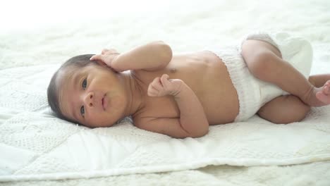 4K-Wide-shot-of-relaxing-sleepy-little-asian-newborn-baby-boy-son-wearing-diaper-lying-down-on-white-bed-in-home-bedroom-and-yawning.-Innocent-newborn-baby-health-care-and-sensitive-skin-concept.