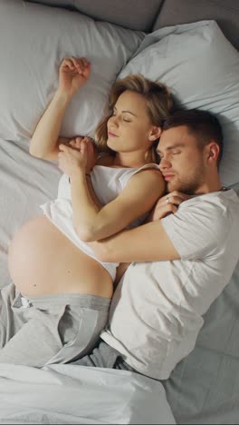 Feliz-pareja-joven-con-mujer-embarazada-durmiendo-juntos-en-la-cama,-dulce-amor-jóvenes-que-se-sostienen-unos-a-otros-mientras-duermen.-Video-De-archivo-con-orientación-vertical-de-la-pantalla-9:16