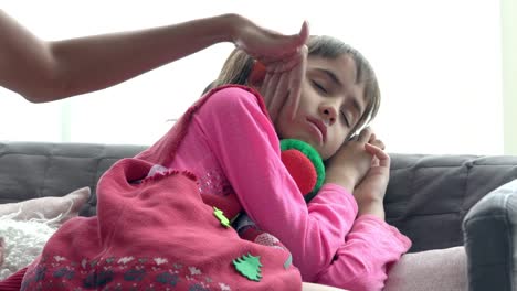 4K-Medium-shot-of-adorable-little-girl-sick-and-sleeping-on-sofa-with-mother-hand-taking-temperature-on-daughter-forehead.-Mother-checking-temperature-of-little-child-daughter-illness-with-fever.