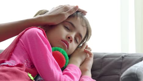 4K-Medium-shot-of-adorable-little-girl-sick-and-sleeping-on-sofa-with-mother-hand-taking-temperature-on-daughter-forehead.-Mother-checking-temperature-of-little-child-daughter-illness-with-fever.