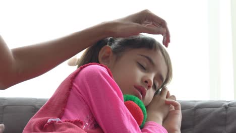 4K-Tiro-medio-de-adorable-niña-enferma-y-durmiendo-en-el-sofá-con-la-mano-madre-tomando-temperatura-en-la-frente-de-la-hija.-Madre-comprobando-la-temperatura-de-la-enfermedad-de-la-hija-pequeña-con-fiebre.