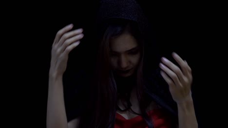 Asian-woman-in-witch-Halloween-costume-opening-black-head-scarf-and-looking-at-camera,-in-slow-motion