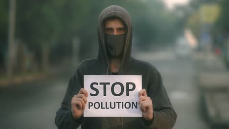 Man-in-respiratory-mask-look-at-camera-backdrop-road-with-banner-stop-pollution