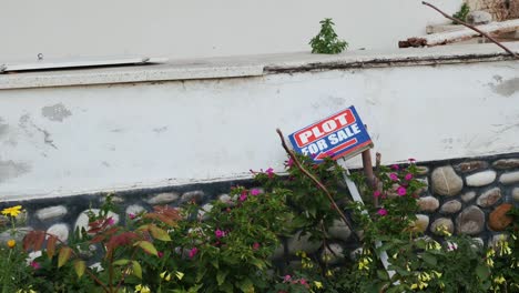 Plot-house-for-sale-sign-on-lawn-with-brick-fence.-Real-estate-concept.