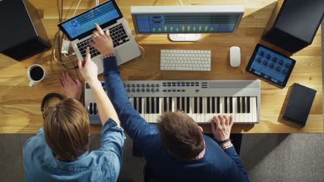 Top-View-von-zwei-Audio-Ingenieuren,-die-in-ihrem-Sonnenstudio-arbeiten.-Sie-spielen-auf-einer-musikalischen-Tastatur-und-Experiment-mit-Sound.