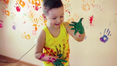 Nahaufnahme-Veiw-niedlichen-kleinen-Jungen-mit-bemalten-Händen-nach-dem-Verlassen-seiner-farbenfrohen-Handabdrücke-an-der-Wand-und-seinen-Daumen-auftauchen.-Junge-Familienglück.-Mutter-Kind-Konzept