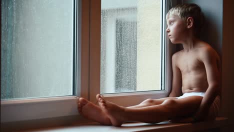 Niño-triste-en-el-alféizar-de-la-ventana-cerca-de-la-ventana