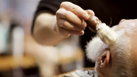 Barber-applies-shaving-cream-on-face-of-old-man-and-prepares-skin-to-shaving