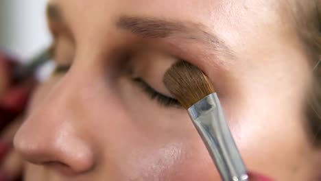 Make-up-artist-applying-light-brown-shadows-on-an-eyelids-with-two-brushes-together,-Close-up-of-a-young-caucasian-woman's-eyes