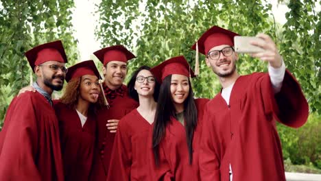 Cheerful-friends-graduating-students-are-taking-selfie-with-smartphone,-young-people-are-posing,-showing-hand-gestures,-making-funny-faces-and-laughing.