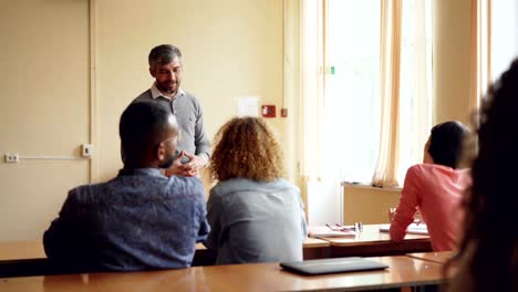 Curious-student-is-raising-hand-and-asking-question,-her-experienced-teacher-is-answering-her-with-friendly-smile.-Profession,-education-and-learning-concept.