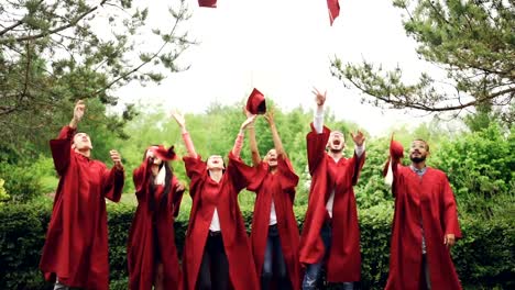 Slow-Motion-der-glücklichen-Absolventen-werfen-Mortarboards-in-Luft,-lachen-und-feiern-Abschluss-am-College-Campus.-Bildung,-Erfolg-und-moderne-Jugendkonzept.